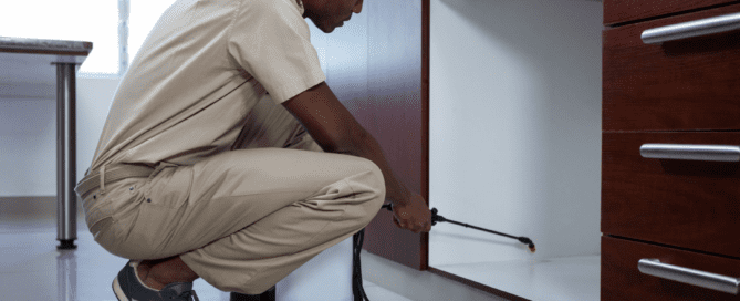 Man in kaki suit spraying kitchen to prevent pests