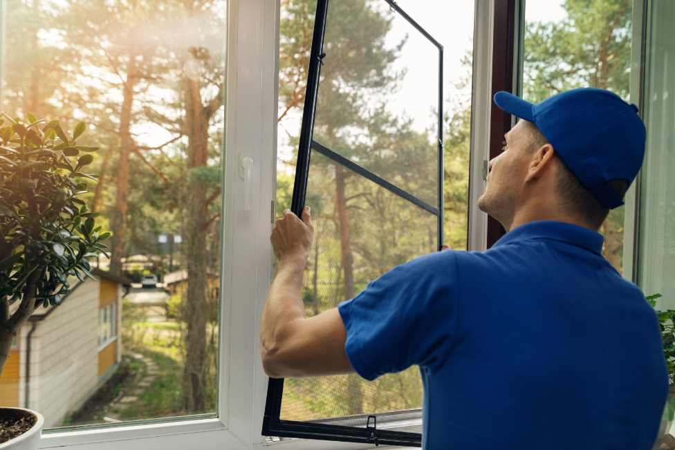A man wearing a blue hat and polo shirt installing window screens