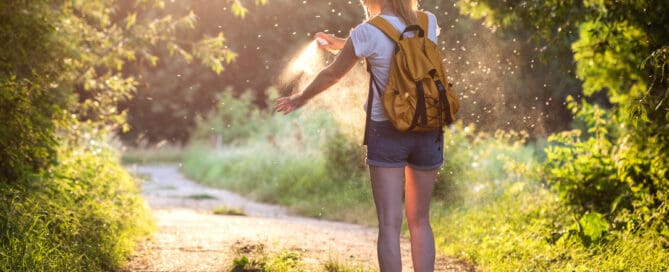 Woman is applying insect repellent against mosquito and tick on her hand during hike in nature. Skin protection against insect bite.