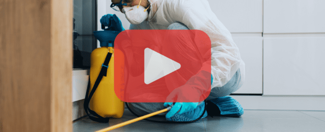 Man wearing safety suit, mask, spraying insecticide on kitchen floor.